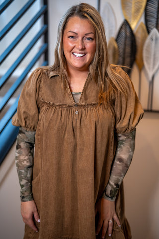 Woman wearing a brown dress with camouflage sleeves in an indoor setting buttercup