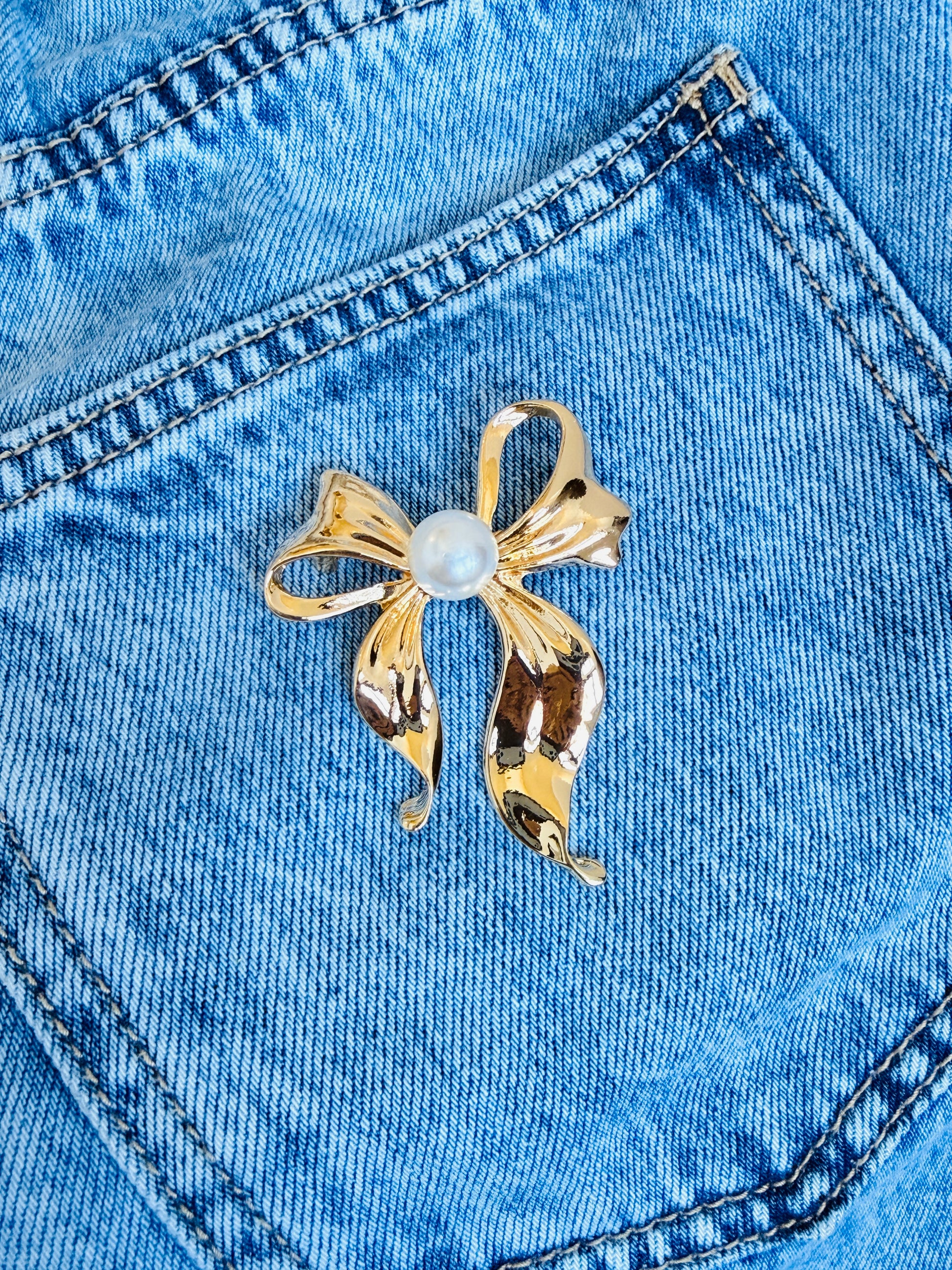 Gold bow-shaped brooch with a central pearl on blue denim fabric