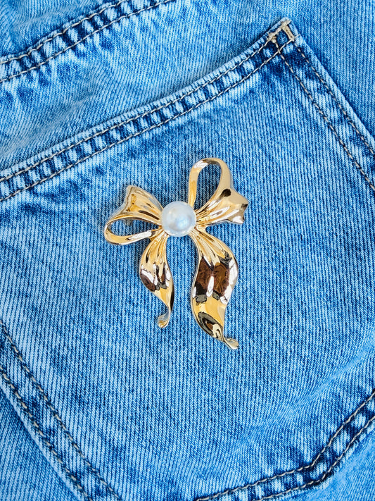 Gold bow-shaped brooch with a central pearl on blue denim fabric