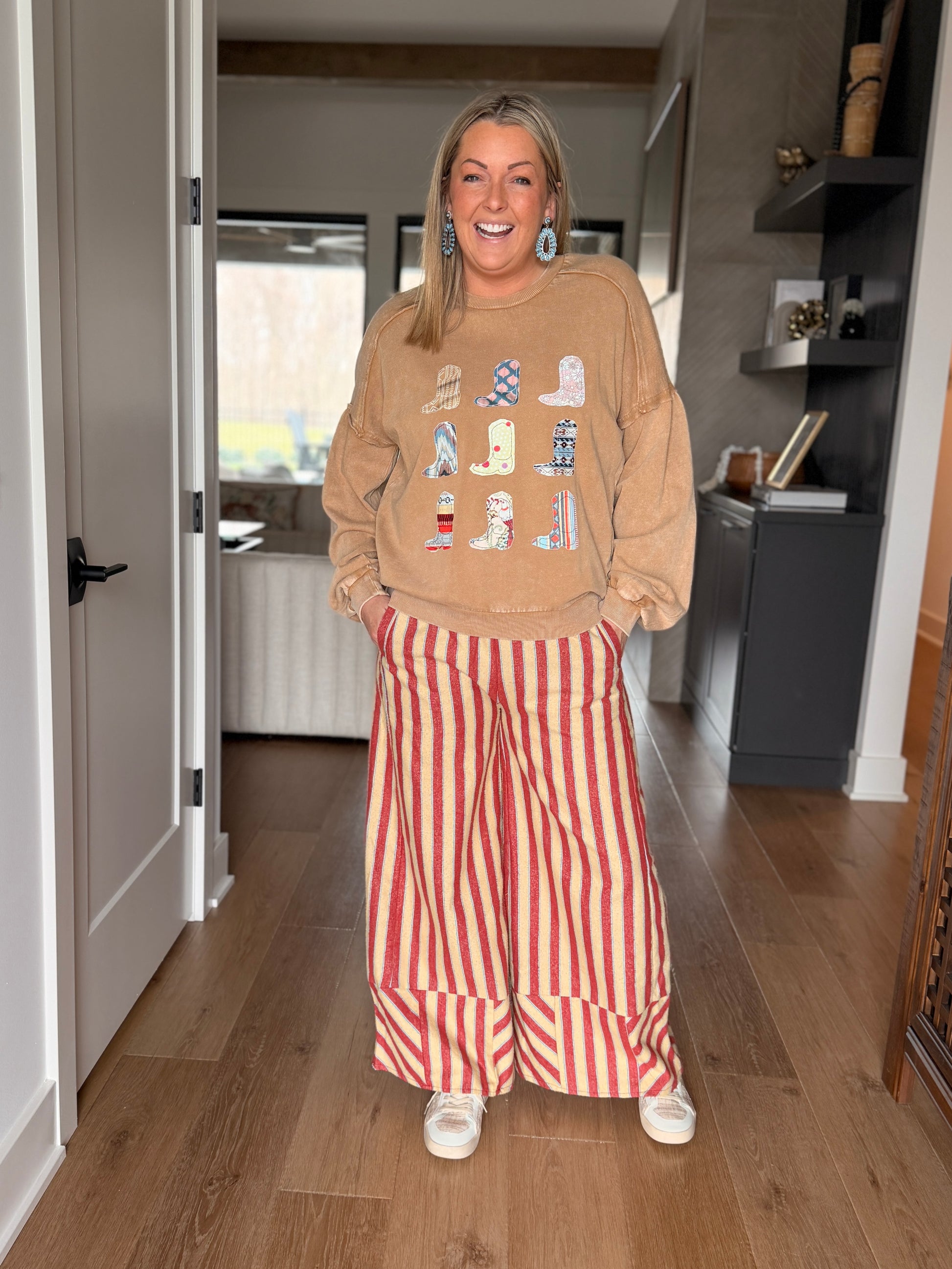 woman standing wearing the striped pants with a tan long sleeve top with cowboy boots on it