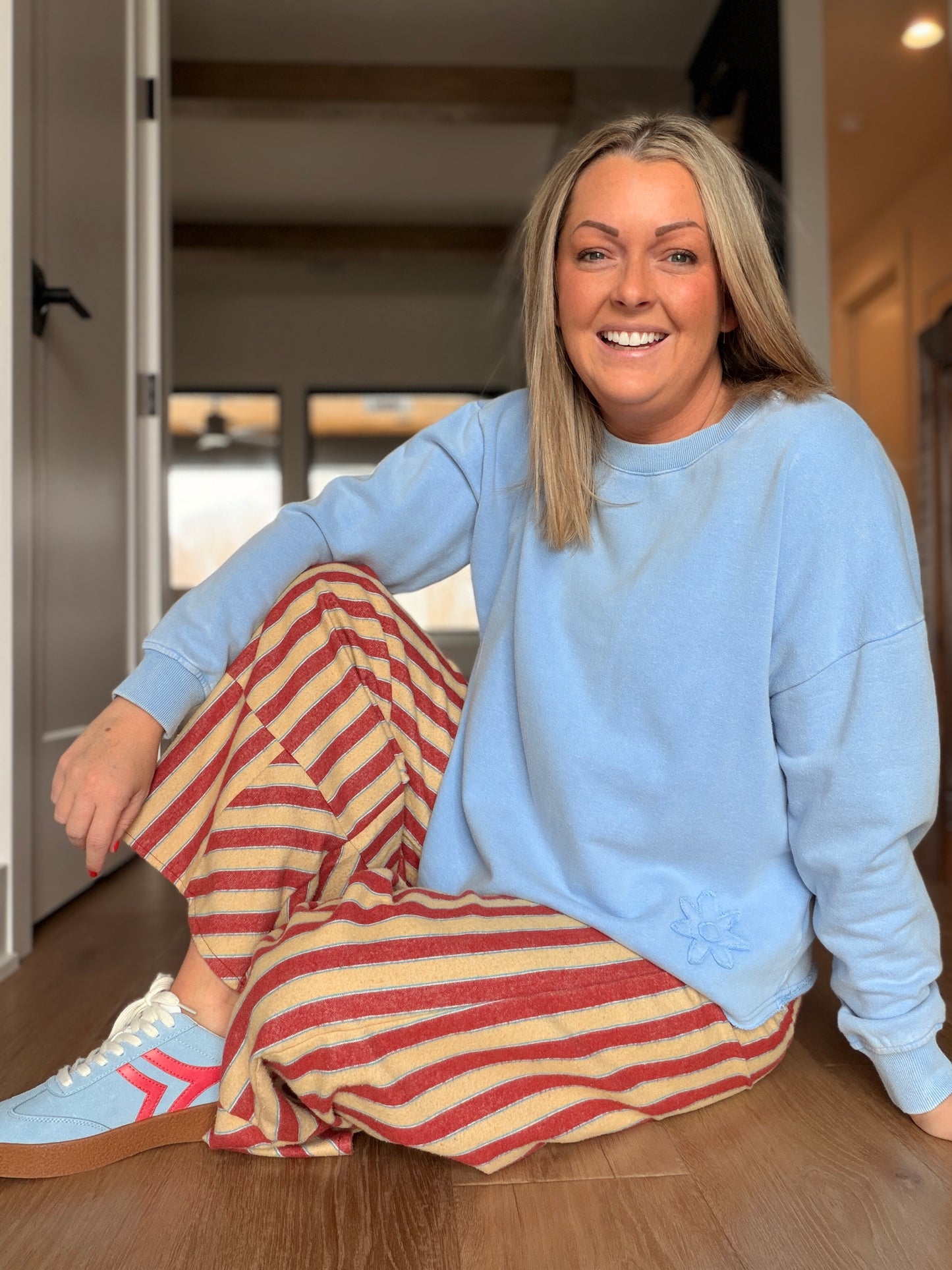 Woman sitting on floor wearing the pants paired with a bright blue floral top from easel