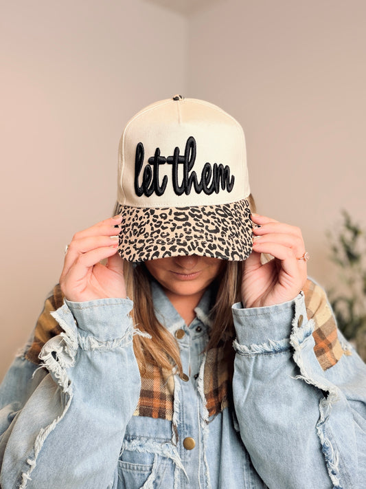 Person wearing a cap with 'let them' text and leopard print brim.