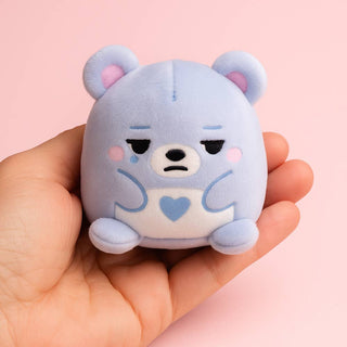 Cute blue plush toy held in a hand against a pink background