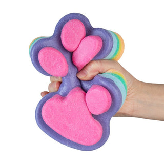Hand squeezing a jumbo rainbow multicolor paw print squishy toy with pink pads